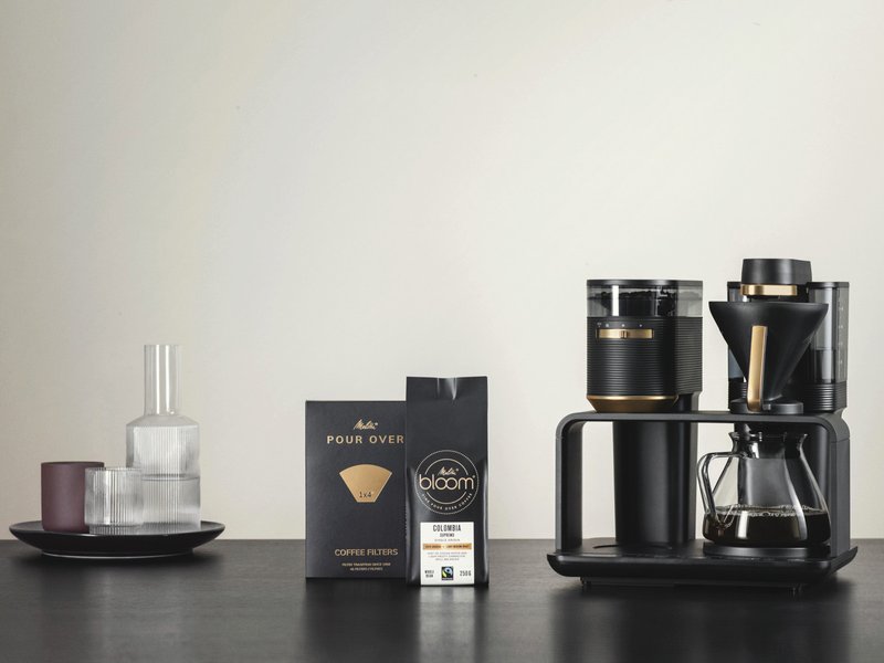 Melitta® EPOS® in an elegant design in black and gold, with the matching Melitta® BLOOM® coffee and Melitta® Pour Over 1X4® filter